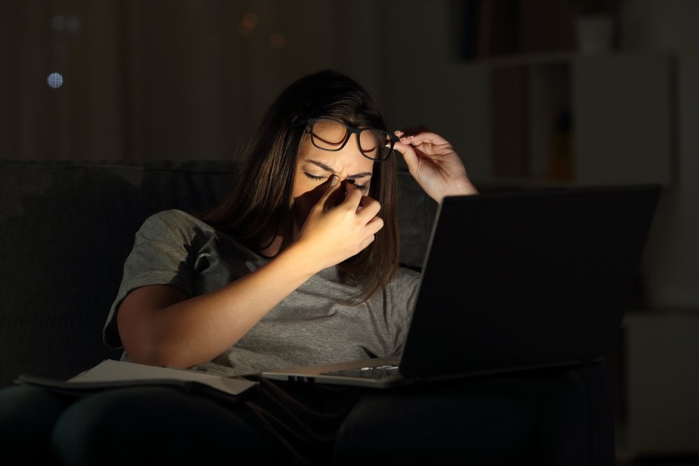 Person rubbing tired eyes at laptop in dim light