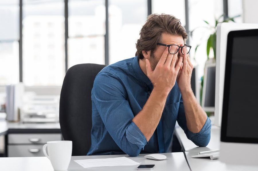 Man rubbing tired eyes at a home office desk